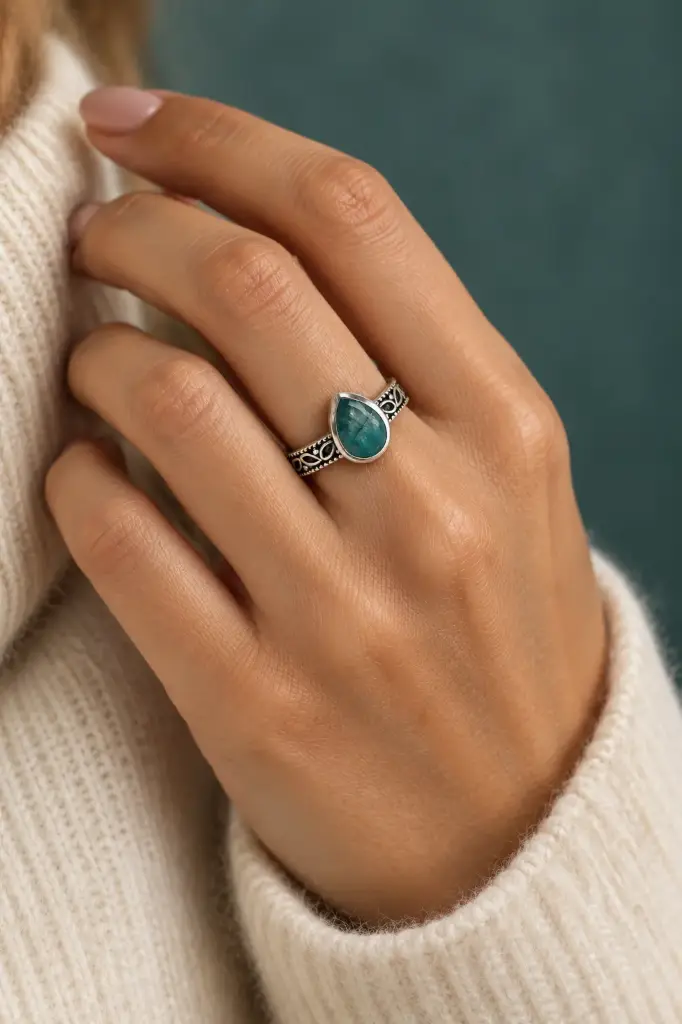An elegant ring featuring a teal-green pear-shaped stone and a finely patterned band.